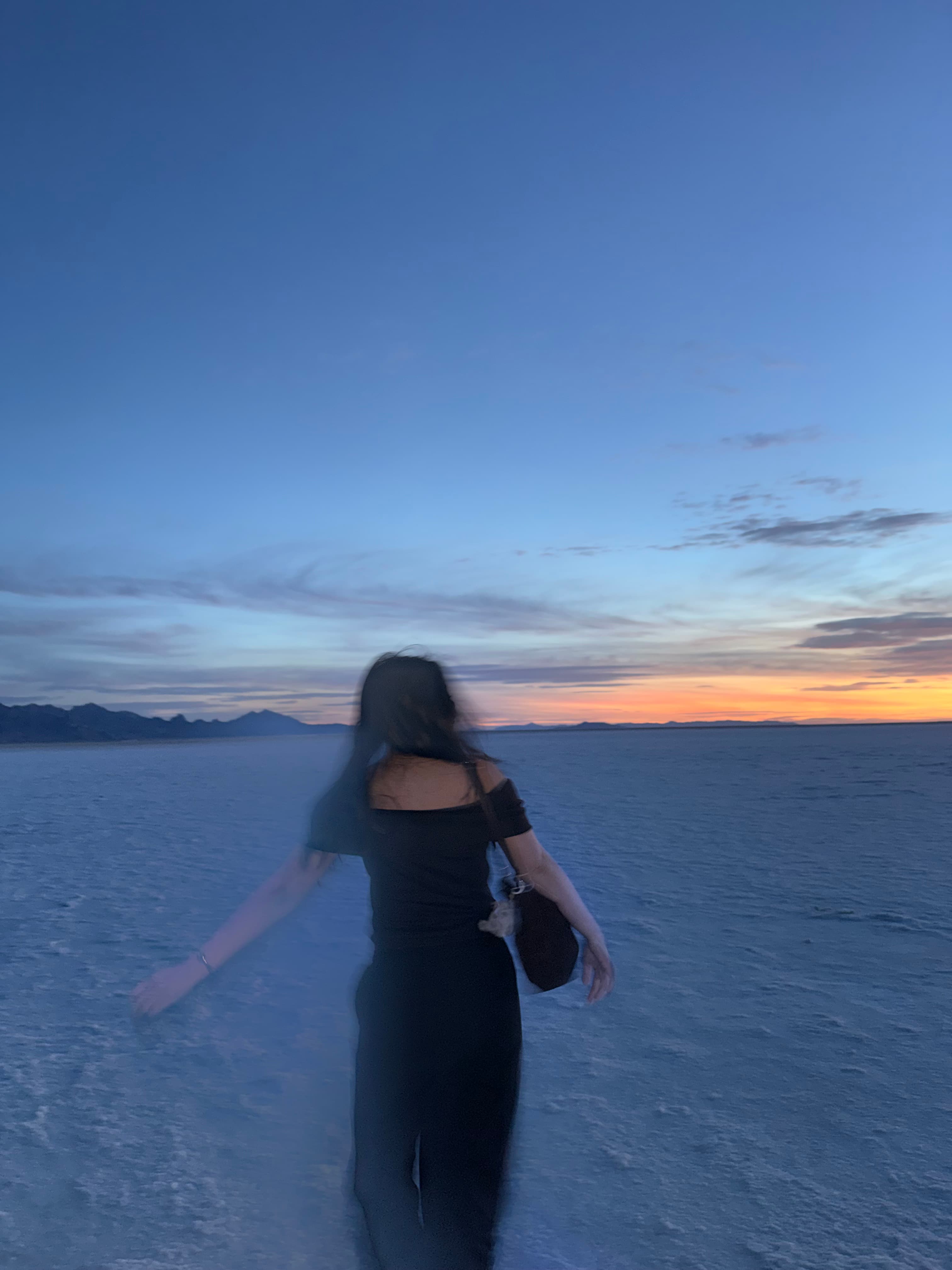 Jesslyn, blurred mid-spin, on white salt flats at dusk with a blue sky and an orange sunset on the horizon