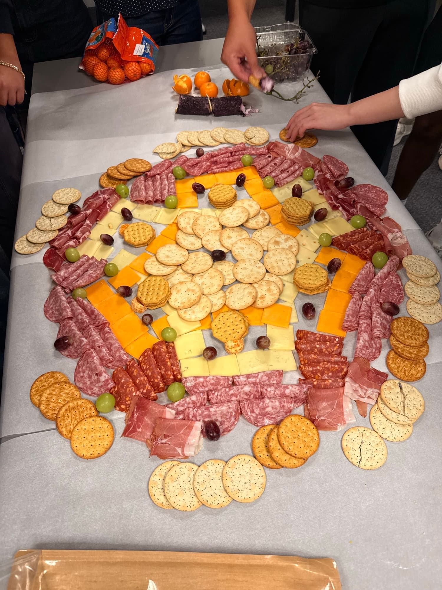 A long table covered in salami, cheese, crackers and grapes laid out in the shape of the Cal Blueprint logo, with hands reaching in